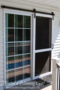 an open sliding glass door on the outside of a house with white siding and black shutters