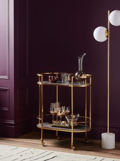 a gold bar cart with wine glasses on it in front of a purple painted wall