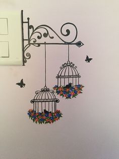 two birdcages with flowers and butterflies hanging from the side of a light switch