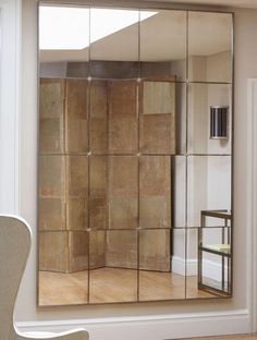 a large mirror sitting on top of a wooden floor next to a chair and window