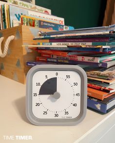 a clock sitting on top of a white table next to stacks of books and magazines