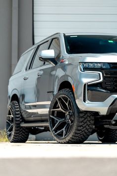 the front end of a silver truck parked in front of a garage door with its lights on