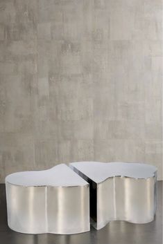 two white tables sitting on top of each other in front of a cement wall and floor