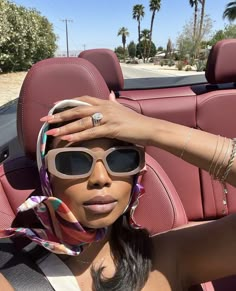 a woman sitting in the back seat of a car wearing sunglasses and a scarf around her head