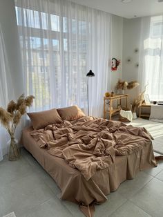 an unmade bed sitting in front of a window with sheer curtains on the windowsill