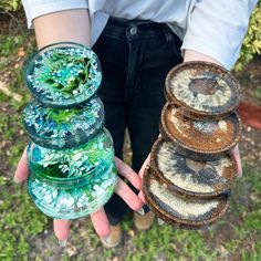 a person holding several glass bowls in their hands with plants growing inside the lids on them