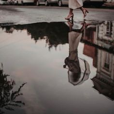 a woman is walking in the rain with an umbrella over her head and she's reflected in the water