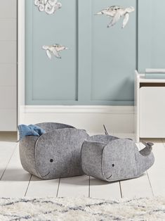 two grey elephant shaped pillows sitting on top of a white floor next to a blue wall