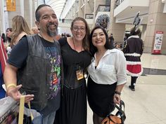 two women and a man are posing for the camera in an indoor shopping mall with other people