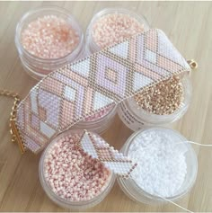 three small containers filled with beads on top of a wooden table next to a gold chain