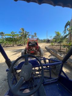 a red jeep driving down a dirt road next to palm trees