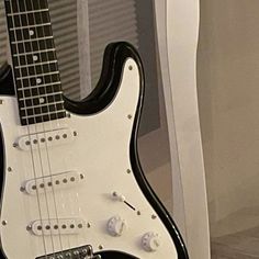 a black and white electric guitar sitting on top of a wooden floor next to a window