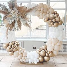 a white and gold balloon wreath on display in front of a window with large windows