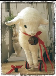 a white stuffed animal with a red ribbon around its neck standing on top of a wooden floor