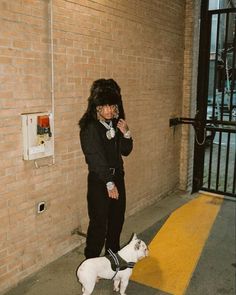 a woman standing next to a white dog on top of a cement floor in front of a brick wall