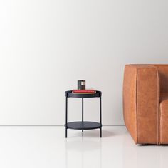 a brown leather chair next to a small table with a cup on it and a white wall in the background