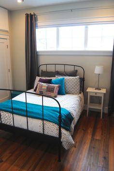 a bed sitting in a bedroom next to a window with blue and white pillows on it