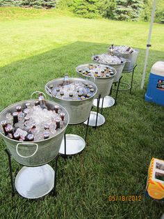 four metal buckets filled with drinks sitting on top of a grass covered field next to an ice chest