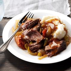 a white plate topped with meat and veggies covered in gravy next to a fork