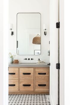 a white bathroom with black and white checkered flooring, large mirror above the sink