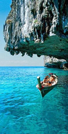 two people in a small boat floating on the water near a large rock formation and cliffs