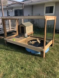 a wooden cage with a bird in it on top of the grass next to a house