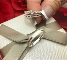 a woman's hand with three wedding rings on top of a gift wrapped in satin ribbon