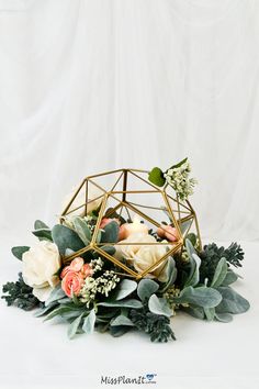 an arrangement of flowers and greenery in a gold geometric vase on a white background