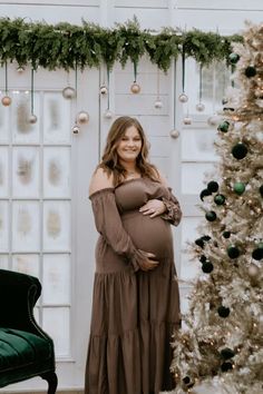 a pregnant woman standing in front of a christmas tree