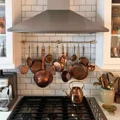 pots and pans are hanging on the wall above an oven in a kitchen with white tiles