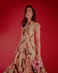 a woman in a dress holding a pink flower and posing for the camera on a red background