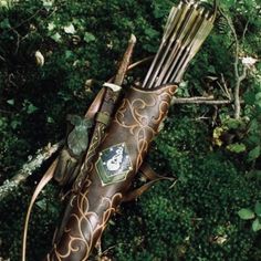 an arrow and bow laying on the ground next to some trees with green leaves around it