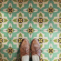 a pair of brown shoes sitting on top of a green and white tiled floor next to a wall