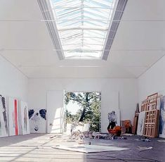 an empty room with paintings on the floor and skylight above it, in front of a large window