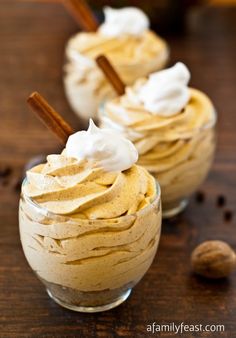 two desserts with whipped cream and cinnamon sticks in glass bowls on a wooden table