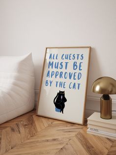 a black cat sitting on top of a bed next to a framed poster with the words, all guests must be approved by the cat