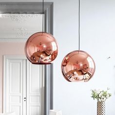 two pink lamps hanging from the ceiling in a room with white walls and chairs around it