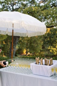 a woman standing next to a table filled with wine glasses and champagne bottles under an umbrella