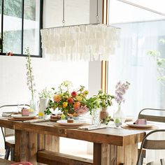 a wooden table topped with lots of flowers next to a tall light hanging from the ceiling