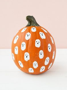 a pumpkin decorated with white ghost faces and heads on it's side, sitting on a table