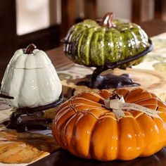 three decorative pumpkins sitting on top of a wooden table next to each other,