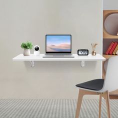 a laptop computer sitting on top of a white desk next to a clock and bookshelf