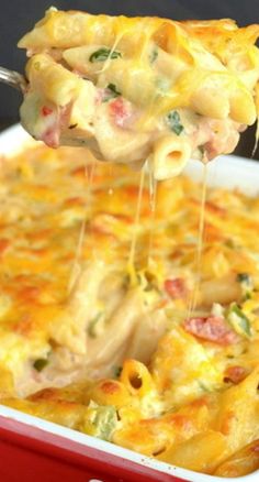 a spoon full of macaroni and cheese being lifted from a red casserole dish