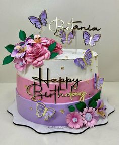 a birthday cake with butterflies and flowers on the top is decorated in pink, purple, and gold