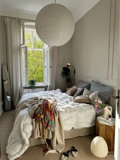 an unmade bed in a bedroom next to a window with a lamp hanging above it