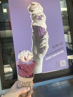 a hand holding an ice cream cone in front of a poster