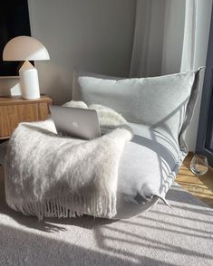 a laptop computer sitting on top of a white blanket next to a lamp and window