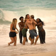 a group of people standing on top of a sandy beach next to the ocean with their arms around each other