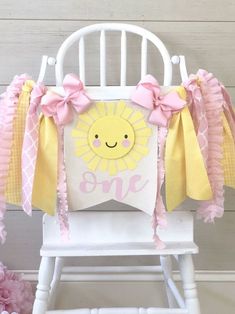 a white rocking chair with pink and yellow decorations on the back that says, one