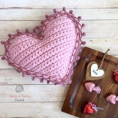 a pink crocheted heart sitting on top of a wooden cutting board next to hearts